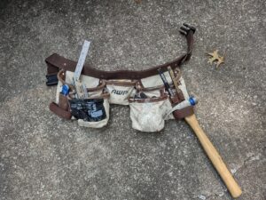 A handyman's tool belt with a hammer and other tools on concrete for Handyashby in Saint Joseph, MO.