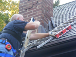 A handyman using a level on a roof ladder near a brick chimney, performing work for Superior Roof Support in Milano, TX.