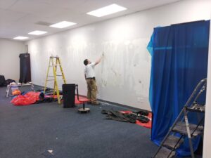 A handyman from IFixdIt Handyman Services in Omaha, NE, scraping old wallpaper or paint from a wall during renovation.