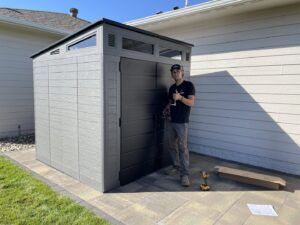 A handyman from Dakota Small Jobs standing proudly next to a newly assembled outdoor storage shed in Sioux Falls, SD.