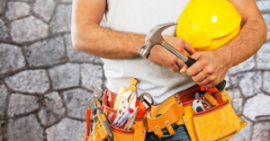 A professional handyman wearing a tool belt and holding a hammer and hard hat, representing B4 It Breaks in Billings, MT.