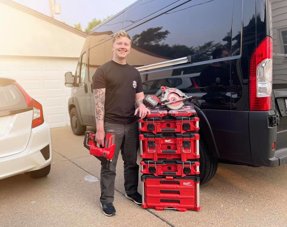 A handyman with a nail gun, toolboxes, and a circular saw next to a work van for Modern Handyman of Minneapolis in Minneapolis, MN.