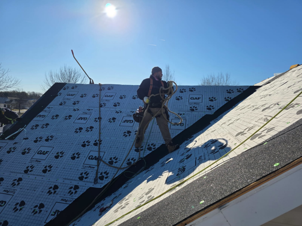 A handyman worker installing roofing underlayment on a residential roof for Bayside Exteriors in Lewes, DE.