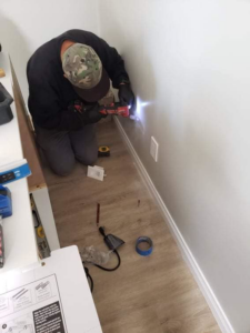 A handyman working on a baseboard and electrical outlet, performing general home maintenance for NH Handyman in San Diego, CA.