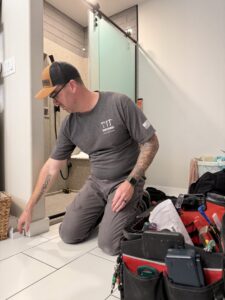 A handyman from Handyworks by Cody English kneeling and working on a bathroom floor installation or repair in Cedar Rapids, IA