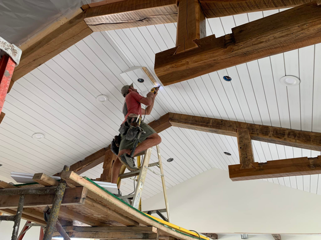 A handyman on a ladder working on ceiling beams and panels in a home in Joseph, OR, by Foursquare Homes Inc.