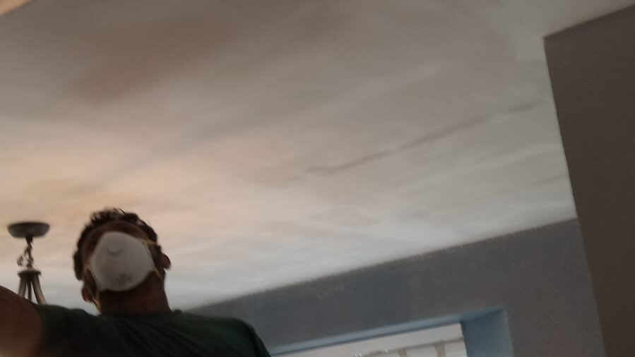 A handyman wearing a mask working on ceiling drywall repair or finishing by Continental Drywall in Aurora, CO