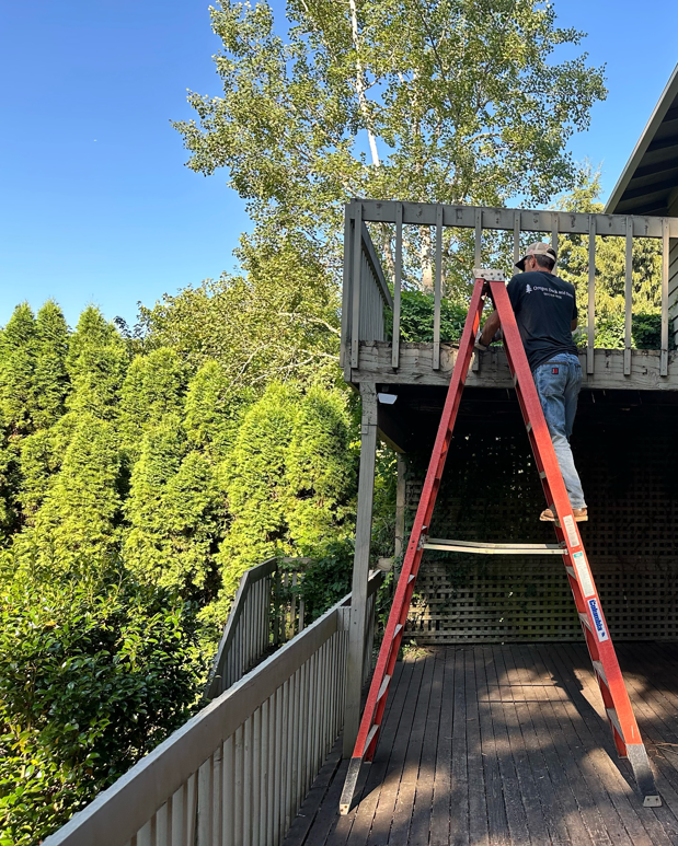 A handyman on a ladder working on a deck railing, providing renovation services for Rosas Construction and Renovation in Dallas, TX.