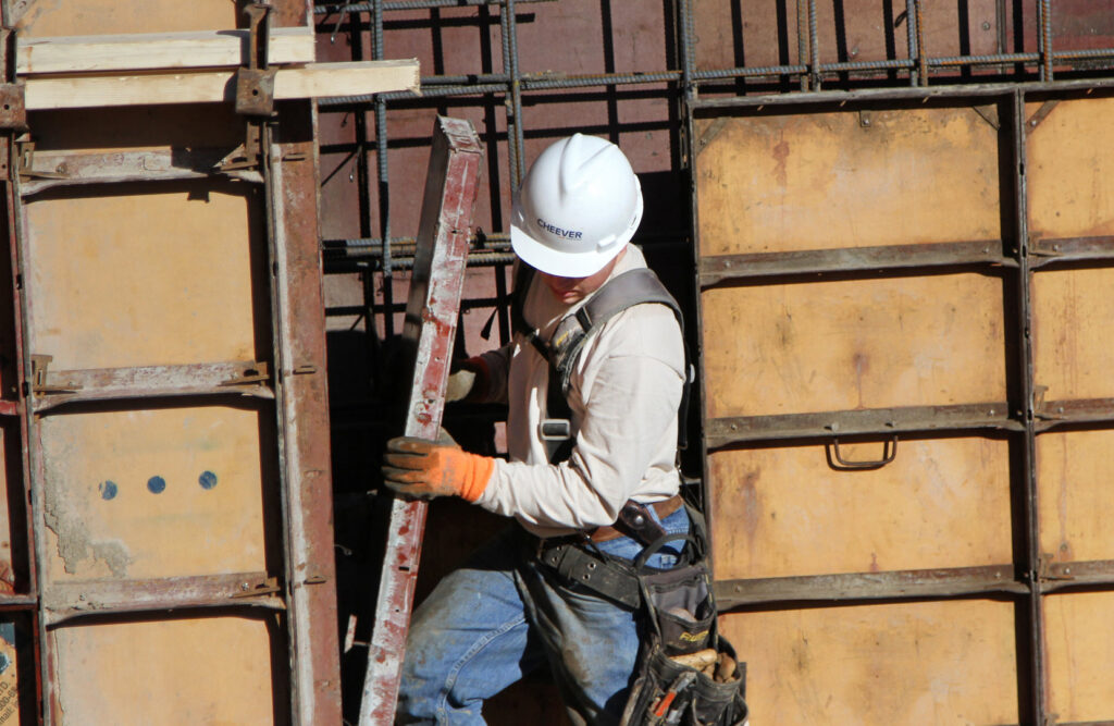 A handyman wearing a hard hat and tool belt working on construction forms at a job site for Cheever Builders in Grand Rapids, MI.