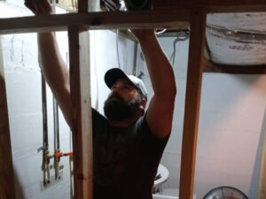 A handyman working on framing and plumbing in a basement or utility room, a service provided by Huntington Home Repair in Huntington, WV.