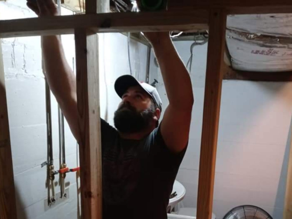 A handyman working on framing and plumbing in a basement or utility room, a service provided by Huntington Home Repair in Huntington, WV.