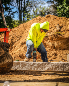 A handyman from White Buffalo Restoration in Nashville, TN, using a power tool to work on concrete blocks for a hardscaping project.