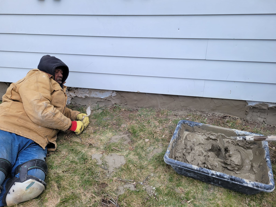 A handyman applying cement to a house foundation during a repair project by Phillips Home Improvements LLC in Philadelphia, PA.
