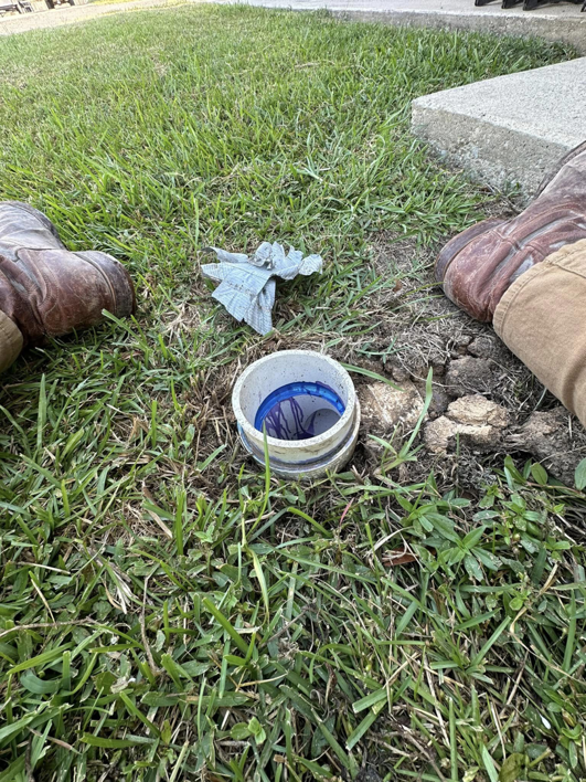 A handyman in work boots inspecting an outdoor drainage pipe for Fix it Fast in Lake Charles, LA.