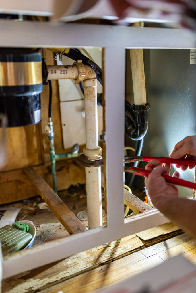 A handyman working on plumbing pipes and a garbage disposal under a kitchen sink for Larry's Appliance Repair in California, MO.