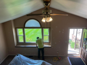 A handyman working on a window sill, with walls prepped for painting and furniture covered, by Honest Help in Fort Wayne, IN