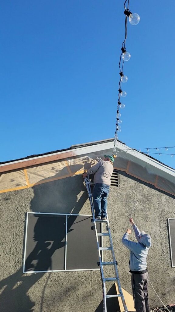 Two handymen from Vegas Handyman Services performing exterior repair and light installation on a house in Las Vegas, NV.