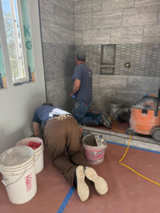Two handymen installing grey wall tiles in a shower during a renovation by Burrell Tile INC in Cottage Grove, OR.
