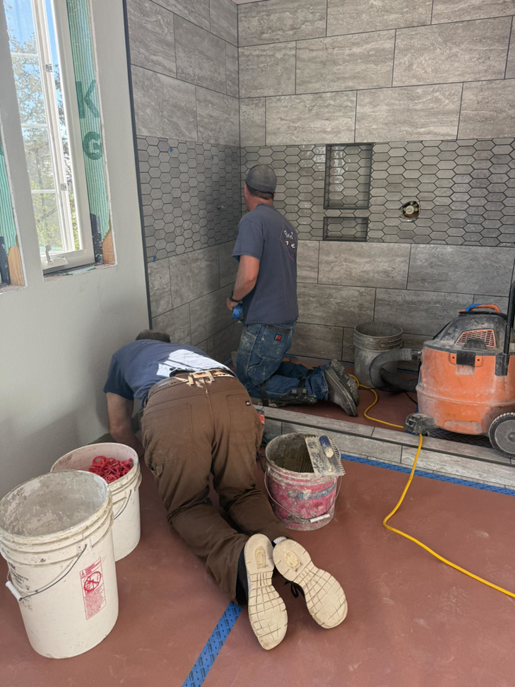 Two handymen installing grey wall tiles in a shower during a renovation by Burrell Tile INC in Cottage Grove, OR.