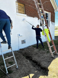 Two handymen from Affordable Home Solutions painting the exterior brick wall of a house in Springfield, PA.