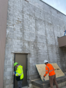 Two handymen from TRM Staffing LLC repairing an exterior brick wall and door in Indianapolis, IN.