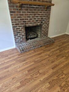 New hardwood flooring installed in a living room with a brick fireplace by Home FREA in Raleigh, NC.