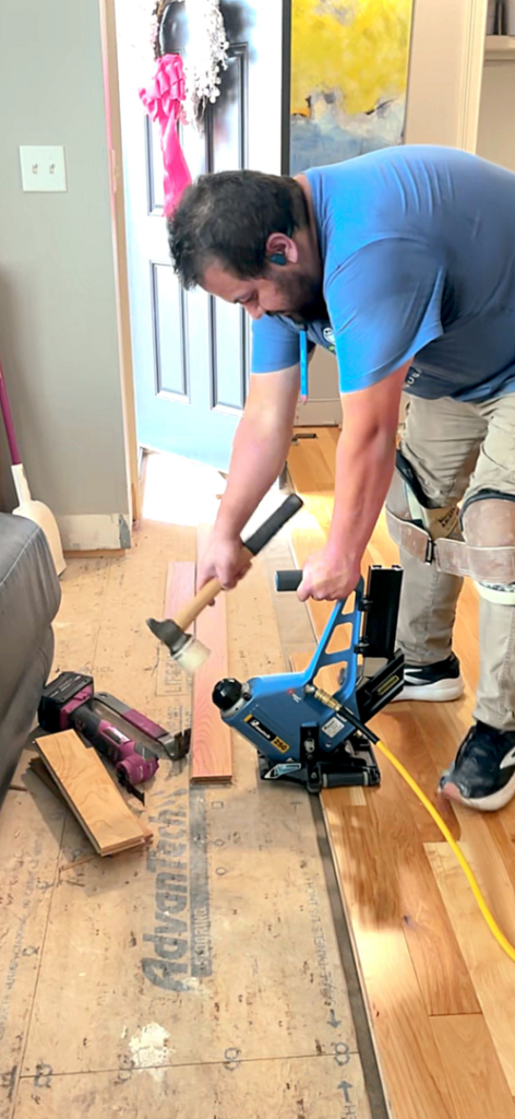 A handyman installing hardwood flooring with a nailer and hammer, a service provided by Floorboys LLC in Lexington, SC.