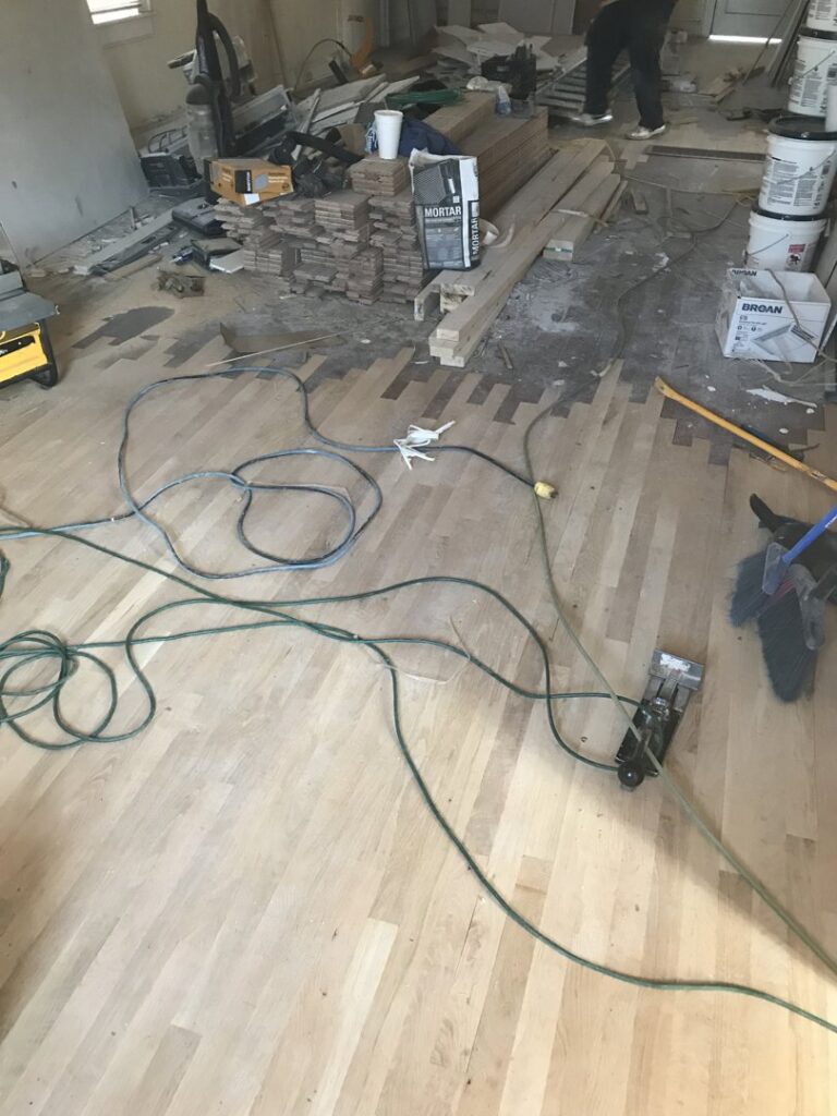 A hardwood floor installation site with planks, tools, and materials, showing work in progress by Franco's Hardwood Flooring in Durham, NC.