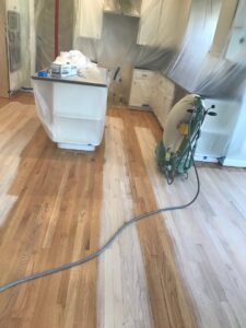 A floor sanding machine working on a hardwood floor in a kitchen, showing a refinishing job by Franco's Hardwood Flooring in Durham, NC.