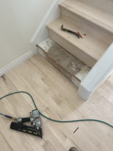 Hardwood stair installation in progress with a nail gun and pry bar by Birdseye Hardwoods LLC in Portland, OR