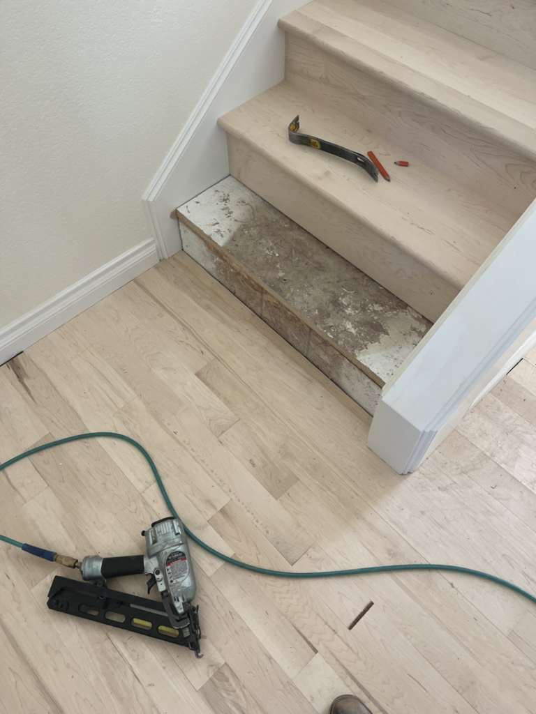 Hardwood stair installation in progress with a nail gun and pry bar by Birdseye Hardwoods LLC in Portland, OR