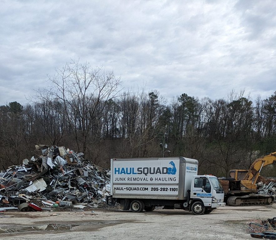 A Haul Squad junk removal truck parked at a scrap metal yard with a large pile of metal in Helena, AL.