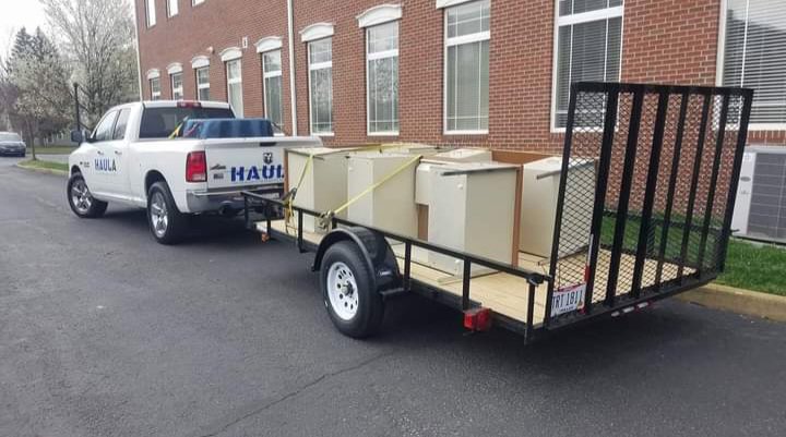 A HAULA Junk Removal truck pulling a trailer loaded with white cabinets, securely strapped for transport in Canton, OH.