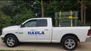A HAULA Junk Removal truck transporting a large green item securely strapped in its bed, demonstrating efficient removal in Canton, OH.