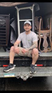A HaulPros team member sitting on the back of a truck partially loaded with furniture, ready for junk removal in Erie, PA.