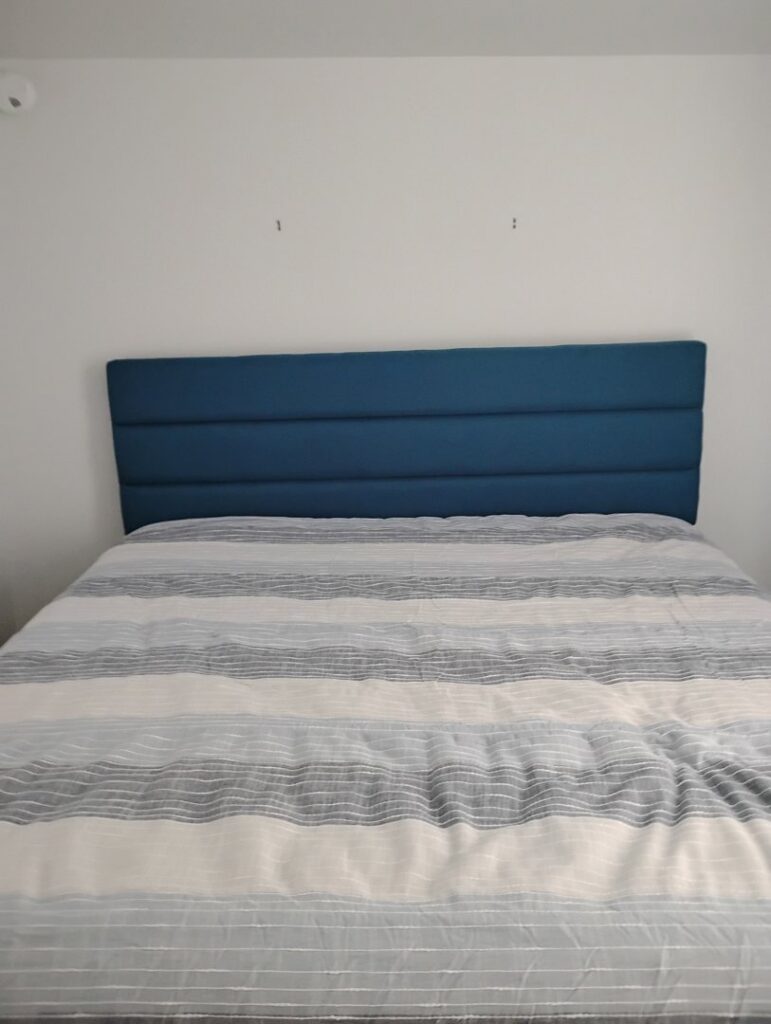 A blue upholstered headboard installed on a white wall, a furniture assembly service provided by McCollister Contracting LLC in New Castle, DE.