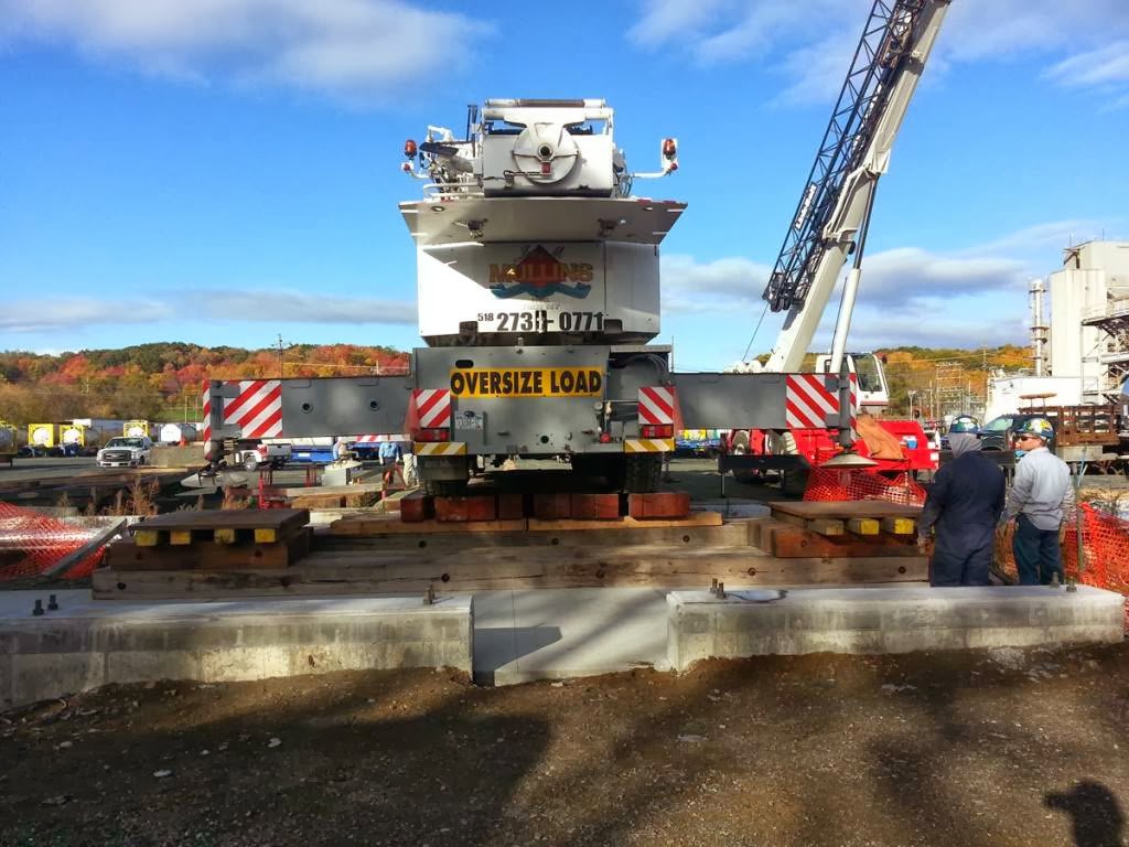 A heavy crane with an 'Oversize Load' sign being set up on a concrete foundation by Mullins Rigging in Green Island, NY