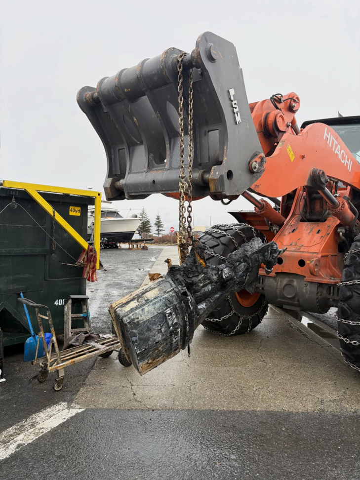 Heavy equipment lifting a large, dirty piece of debris next to a dumpster, showing junk removal by Alaska Waste in Anchorage, AK.