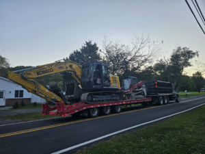 Heavy construction equipment, including an excavator and skid steer, being transported by Composite Pools USA in Newfield, NJ.