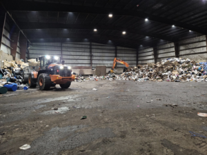 Heavy machinery, including a front loader and excavator, moving large piles of junk inside a facility for Voyager Trucking in Newark, NJ