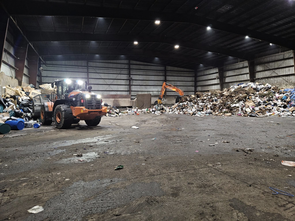 Heavy machinery, including a front loader and excavator, moving large piles of junk inside a facility for Voyager Trucking in Newark, NJ
