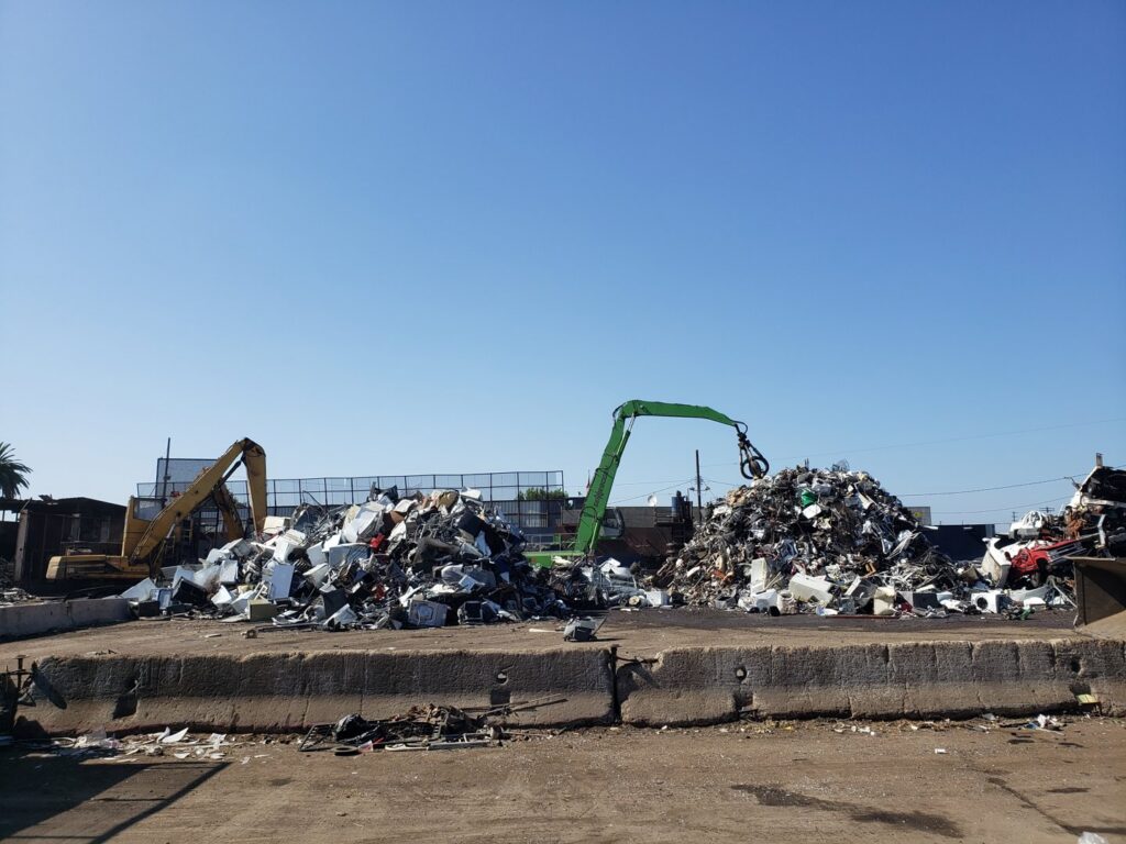Heavy machinery moving large piles of scrap metal and appliances at SA Recycling - Long Beach Ave in Los Angeles, CA.