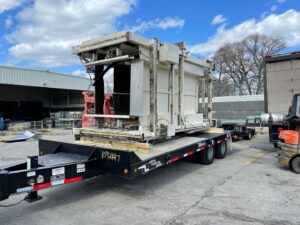 Large industrial machinery loaded onto a flatbed trailer for transport by Remove Recycle Remarket in Troy, MI.