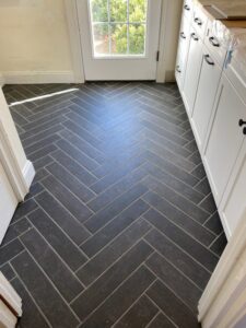 Newly installed dark herringbone tile flooring in an entryway, a project by Pink Rose Home Service in Rochester, NY.