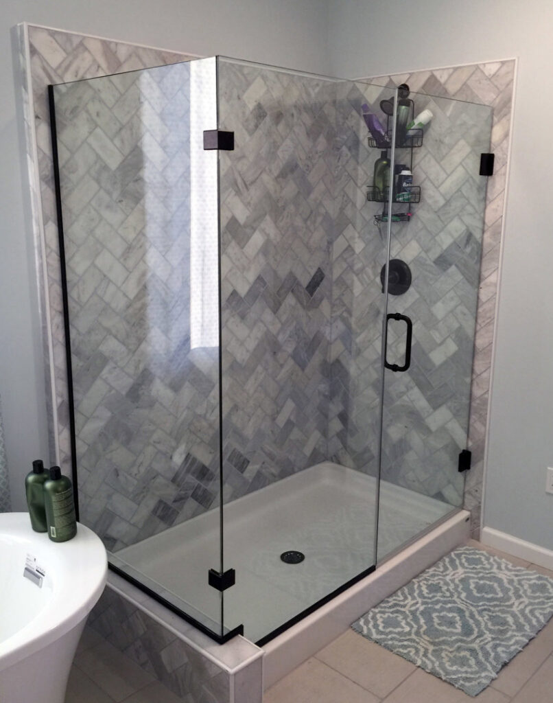 A modern shower with herringbone tile walls and sleek black fixtures, part of a bathroom remodel by Lehigh Shower Glass in Bethlehem, PA
