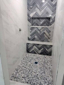 A newly tiled shower with herringbone pattern and pebble floor by Indy Renovation in Indianapolis, IN.