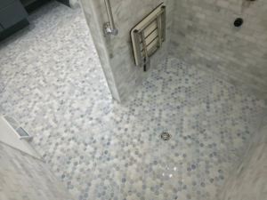 A clean hexagonal tile shower floor with a fold-down seat installed by Tyler the Tiler in Jefferson, WI.