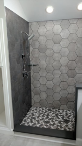 Walk-in shower featuring dark grey hexagonal wall and floor tiles by Coastal Contracting Services Inc., Virginia Beach, VA.