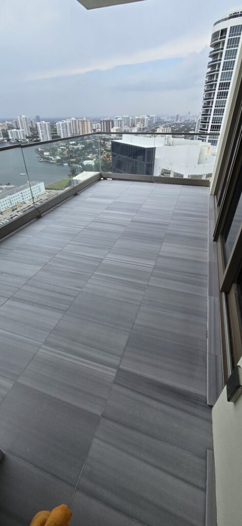 A high-rise balcony with modern grey tiled floors and a glass railing, installed by Cornerstone Services Management in Miami, FL.