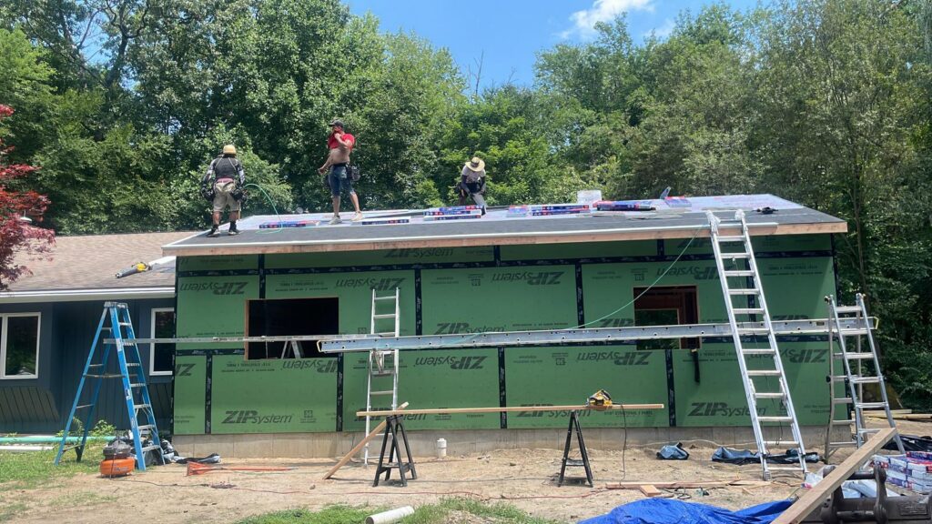 Construction workers on a roof during a home addition project, with green sheathing on the walls by Usa Construction of Danbury LLC in Danbury, CT.